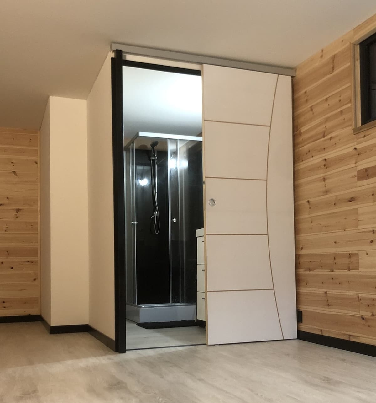 Intérieur de cabanon aménagé : lambris bois et salle d’eau avec porte coulissante