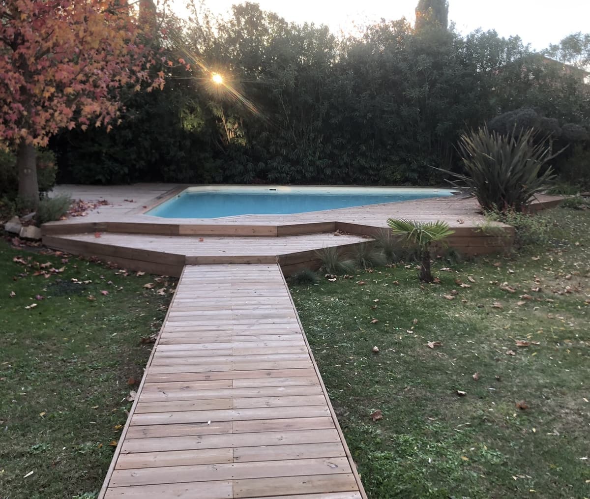 Plage de piscine en bois avec passerelle traversant la pelouse