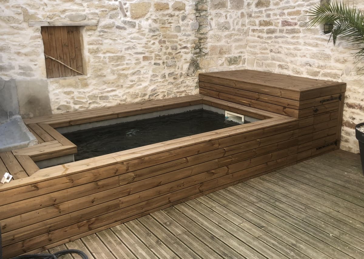 Bassin habillé de bois contre un mur en pierre, avec banquette