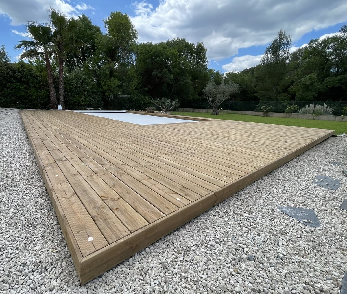 Grande terrasse bois sur gravier autour d’une piscine couverte