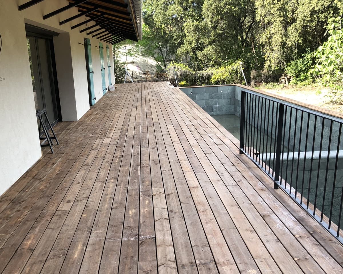 Terrasse bois le long d’une maison avec bassin et garde-corps métal
